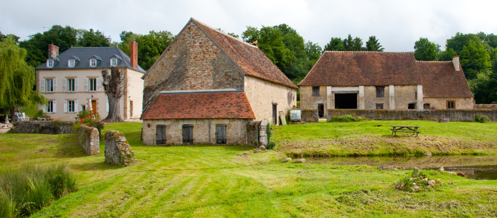 The full property seen from a distance: the house, barns and cottage among trees